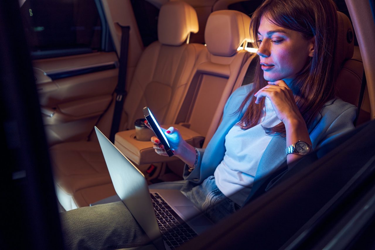 Woman using mobile phone and laptop in car